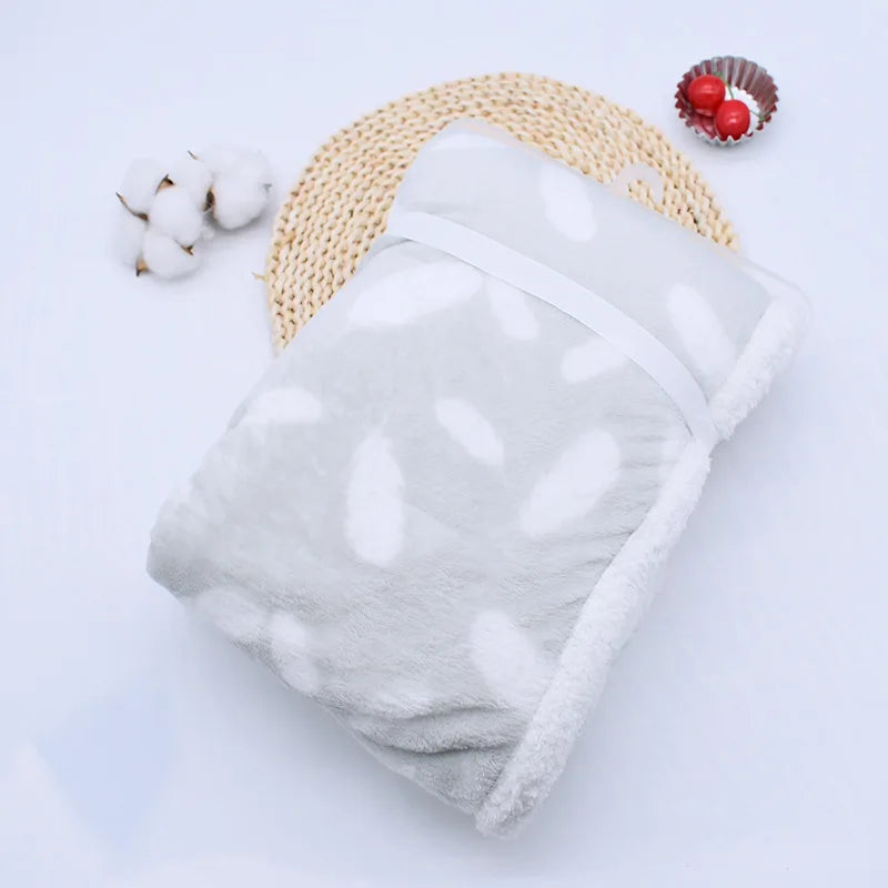 couverture bébé thermique pliée motifs plumes gris pâle blanc présenté sur naperon