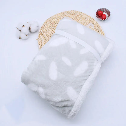 couverture bébé thermique pliée motifs plumes gris pâle blanc présenté sur naperon