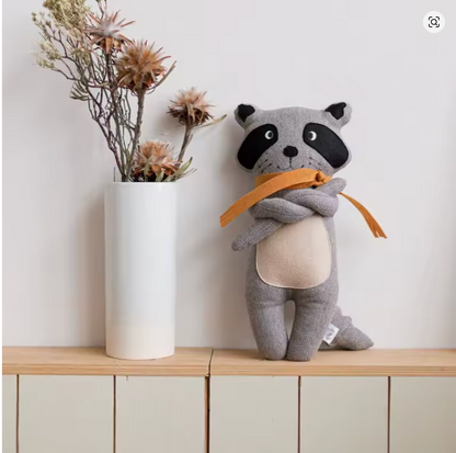 doudou bebe animal raton laveur gris debout sur tablette mains croisées